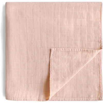 Mushie Muslin Swaddle Blanket in blush color, showcasing a soft, textured fabric with a square pattern and a folded corner.