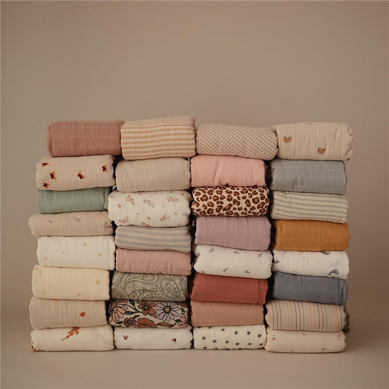 Mushie Muslin Swaddle Blankets in various colors and patterns neatly stacked, highlighting the blush variant.