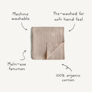 Mushie Muslin Swaddle Blanket in blush, made of 100% organic cotton, with text highlighting its softness and multi-use function.