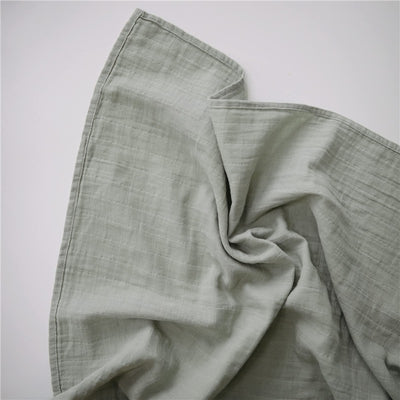 Organic cotton muslin swaddle blanket in sage color, crumpled fabric texture visible against a white background.