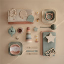Mushie Organic Cotton Muslin Swaddle Blanket in sage, surrounded by various feeding accessories and toys on a neutral backdrop.