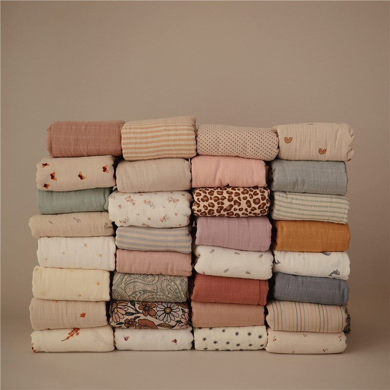 Organic cotton muslin swaddle blankets in various colors and patterns, neatly stacked.
