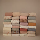 Organic cotton muslin swaddle blankets in various colors and patterns, neatly stacked.