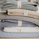 Stack of Mushie hooded towels in baby blue, gray, cream, and white, featuring labels with the brand name.