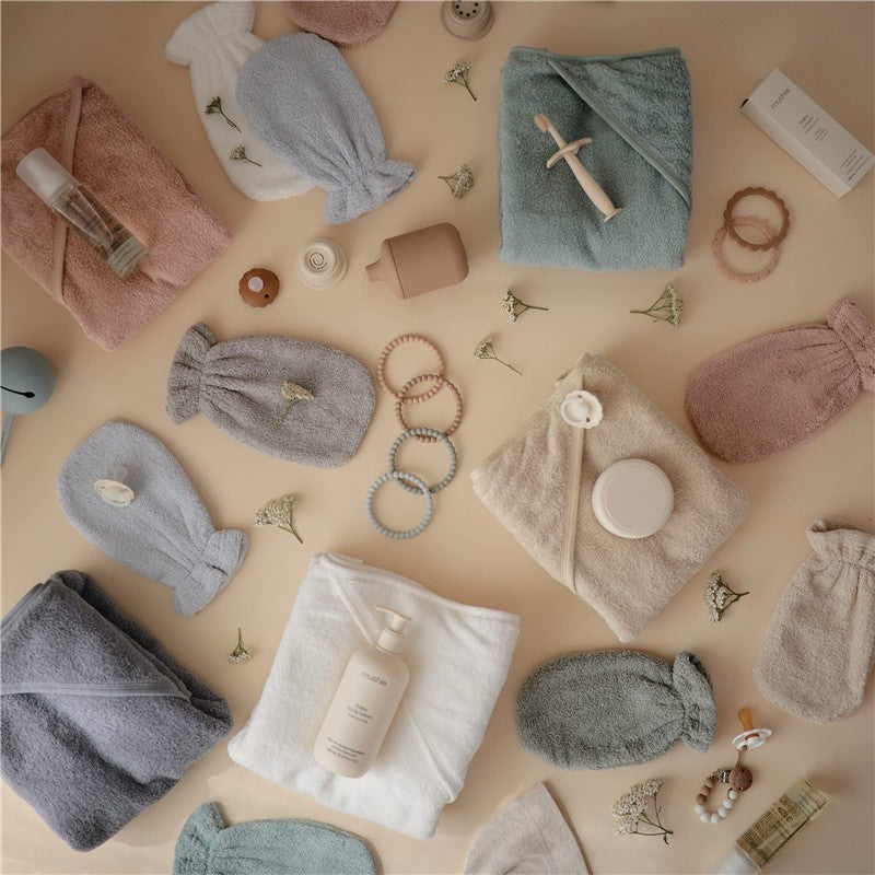 Mushie Hooded Towel in Baby Blue surrounded by pastel-colored towels, bath accessories, and small decorative items.