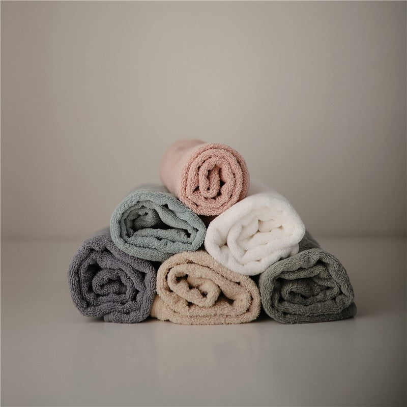 Hooded towels in various colors, including moss green, stacked neatly; soft texture and rolled design evident.