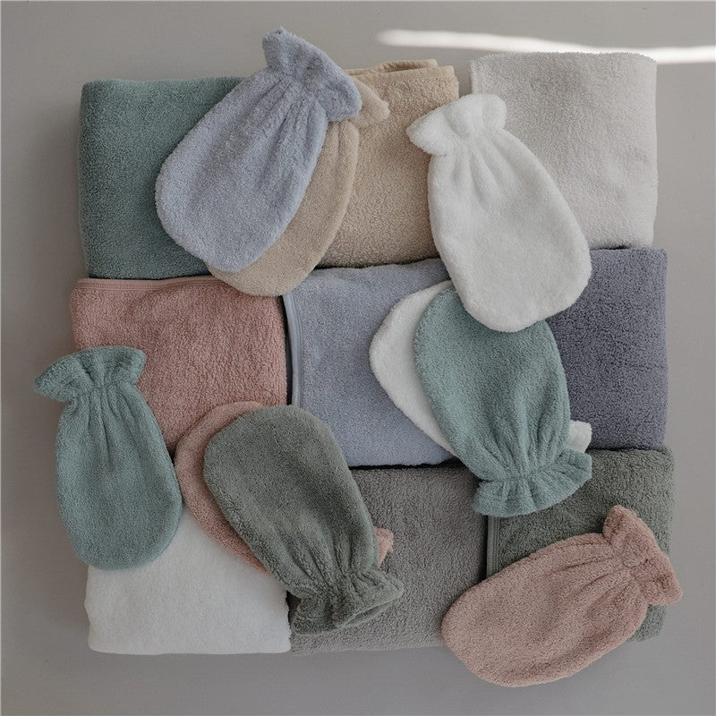 Mushie hooded towels and wash mitts in various soft colors, arranged neatly on a light background.