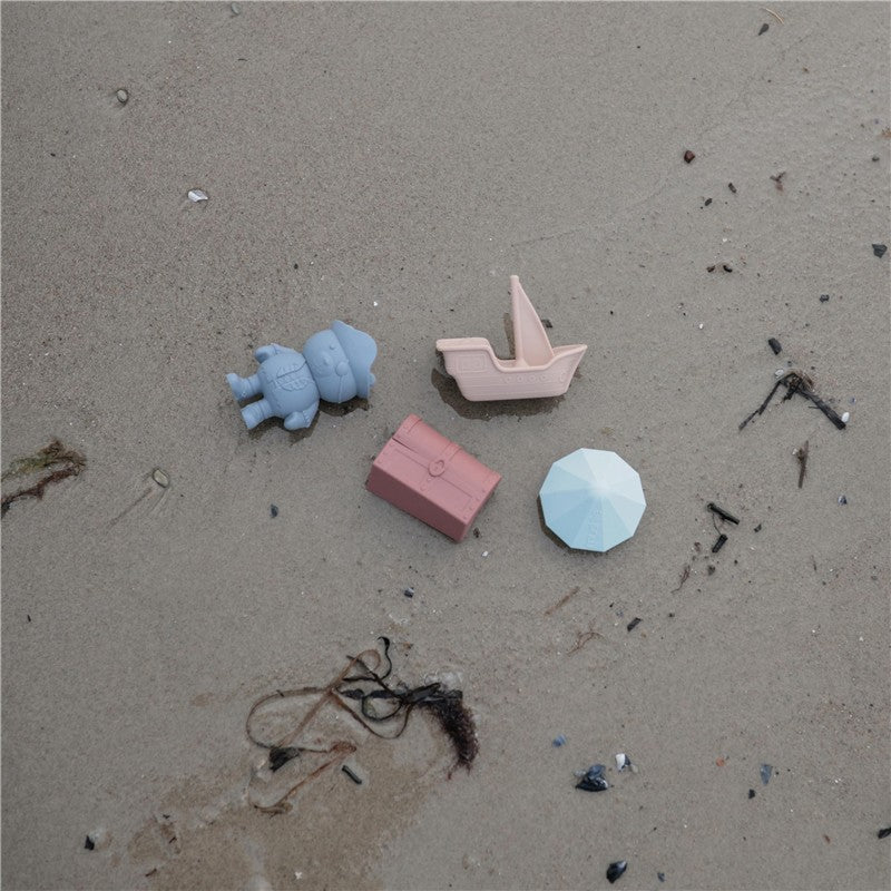 Mushie Pirate Mold Free Bath Play Set including a blue pirate figure, pink boat, pink treasure chest, and blue umbrella on sand.