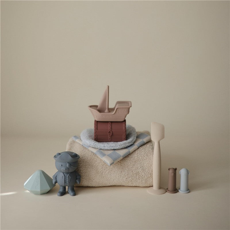 Mushie Pirate Mold Free Bath Play Set features a pirate ship and treasure chest toy, additional characters, and shapes on a towel.