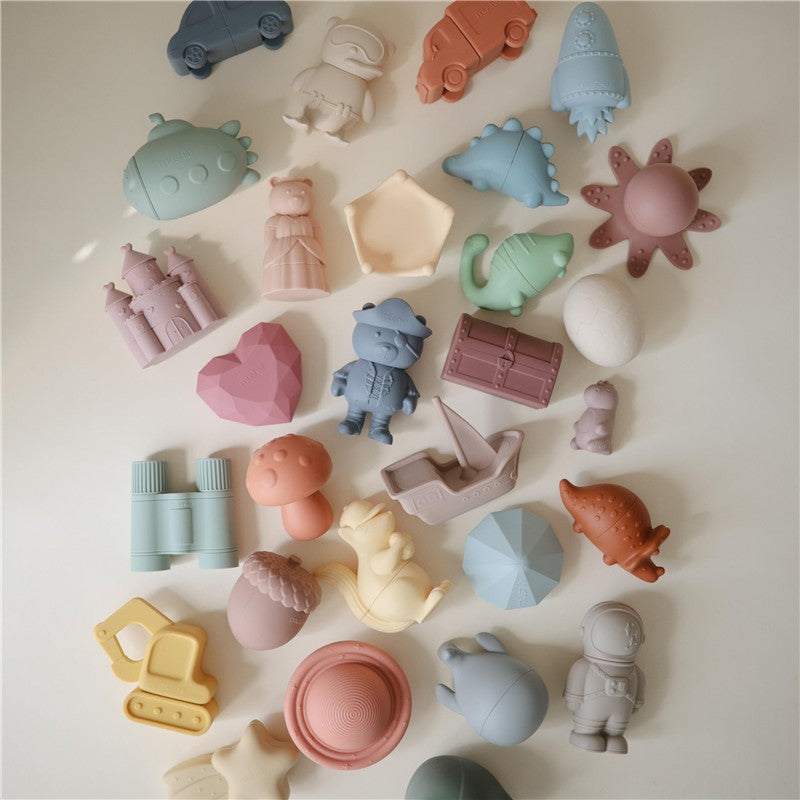 Colorful, silicone bath toys in various shapes, including animals, vehicles, and a treasure chest, from the Mushie Pirate Mold Free Bath Play Set.