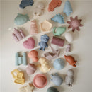 Colorful, silicone bath toys in various shapes, including animals, vehicles, and a treasure chest, from the Mushie Pirate Mold Free Bath Play Set.
