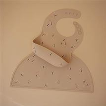 Silicone baby bib in beige with cheerful bee patterns, featuring an adjustable neck and a catch pocket for food spills.