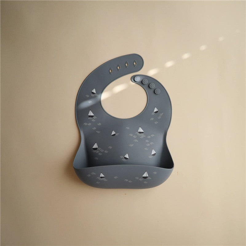 Silicone baby bib in gray featuring a boat design, with a wide pocket for catching crumbs and spills.