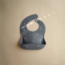 Silicone baby bib in gray featuring a boat design, with a wide pocket for catching crumbs and spills.