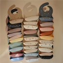 Silicone baby bibs in various colors and prints, including designs with boats and whimsical patterns, stacked together.