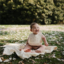 Baby wearing a Mushie silicone bib with bows, sitting on a blanket outdoors, smiling.