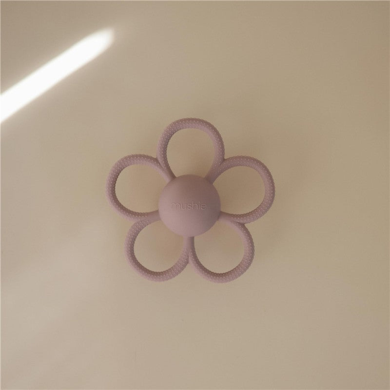 Mushie Daisy Rattle Teether in soft lilac, featuring a flower shape with textured rings and a central ball.