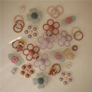 Mushie Daisy Rattle Teether in soft lilac, surrounded by various colorful silicone flower-shaped teethers and accessories.