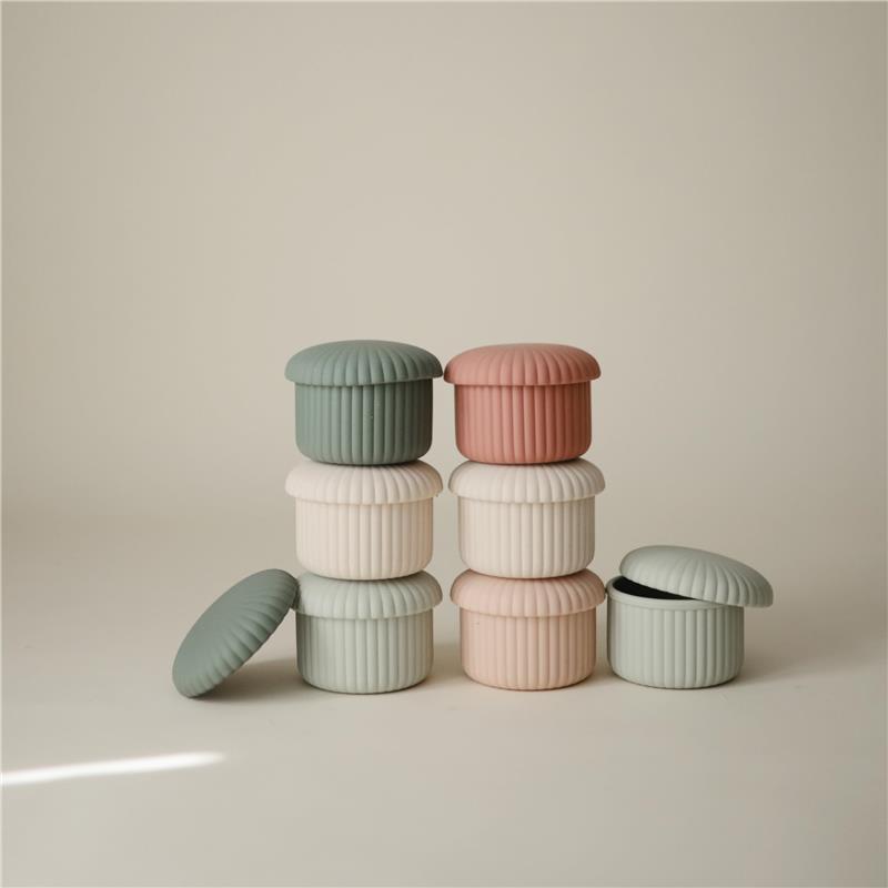 Mushie Silicone Baby Food Containers in pink, green, and white stacked with one lid off, showcasing their ribbed design.