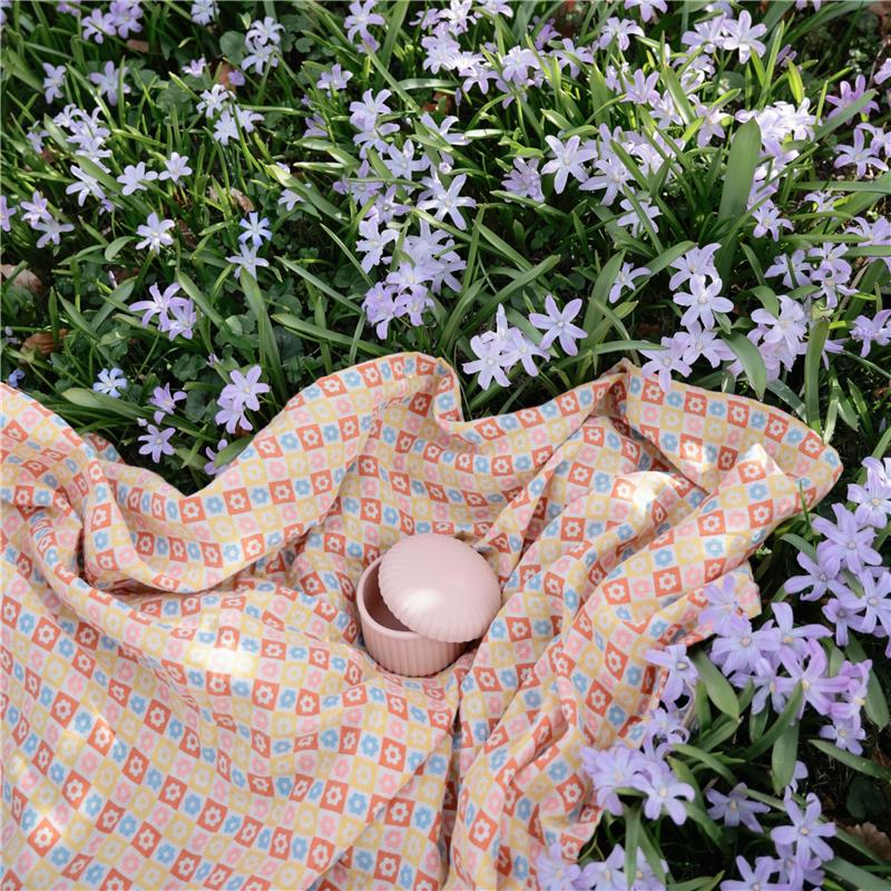 Mushie silicone baby food container in pink, placed on colorful fabric among light purple flowers.