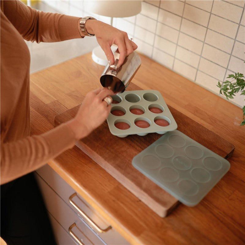 Mushie Baby Food Freezer Tray in Cambridge Blue being filled with food from a stainless steel container on a wooden countertop.