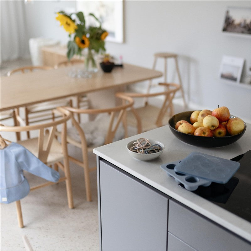 Mushie Baby Food Freezer Tray in Cambridge Blue rests on a kitchen counter next to a bowl of apples and rubber bands.