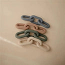 Silicone teether toy in varying pastel colors, stacked in a chain-like formation on a beige surface.