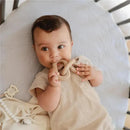 Baby happily chewing on a beige silicone teether toy while lying on a soft, light-colored surface.