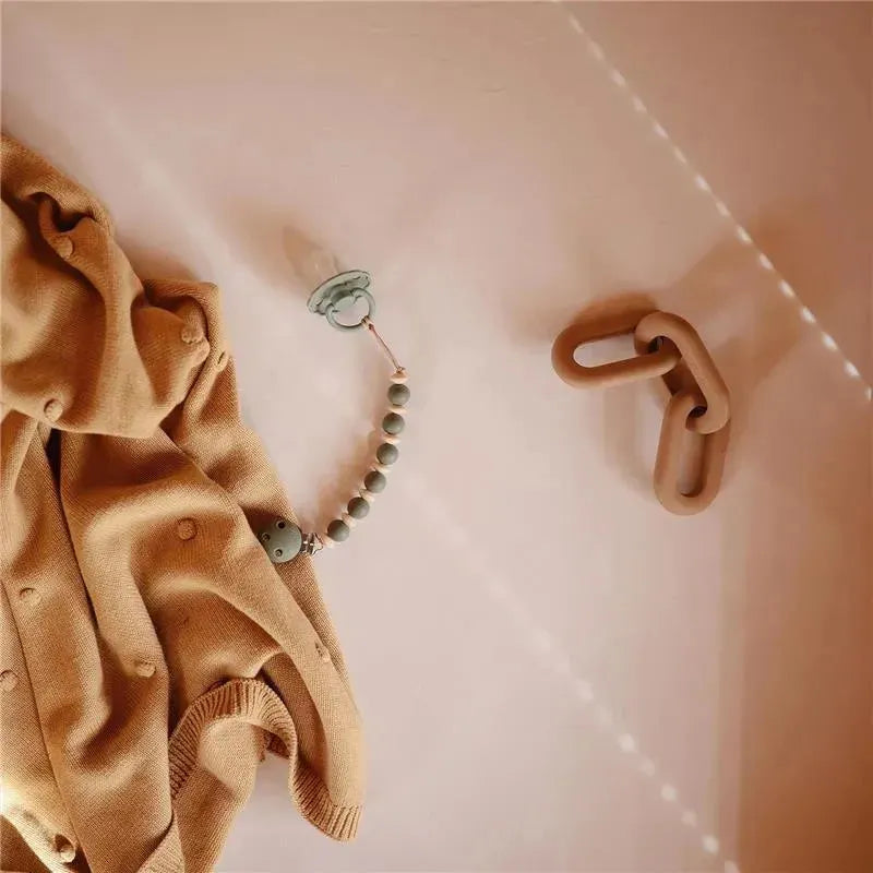 Silicone teether toy featuring colorful beads, a soft animal shape, and a pacifier clip, lying on a beige blanket.