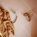 Silicone teether toy featuring colorful beads, a soft animal shape, and a pacifier clip, lying on a beige blanket.
