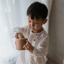 Child in a white shirt interacting with a natural-colored silicone snack cup, exploring its contents.