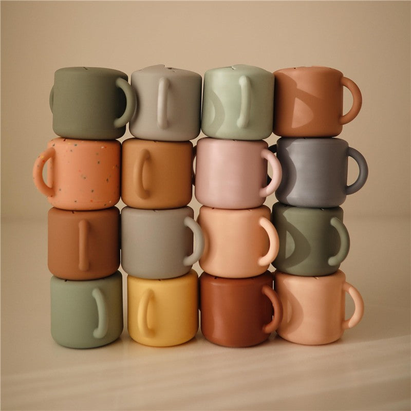 Mushie Silicone Snack Cups in various colors stacked neatly, showcasing their soft, matte finish and playful designs.