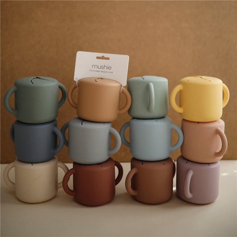 Mushie Silicone Snack Cups in various pastel colors, stacked with a label displaying the product name.