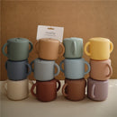 Mushie Silicone Snack Cups in various pastel colors, stacked with a label displaying the product name.