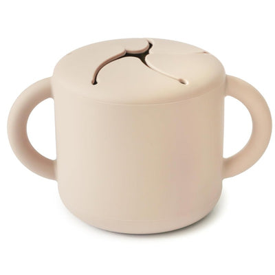 Mushie Silicone Snack Cup in shifting sand color with two handles and a slotted lid for easy snacking.