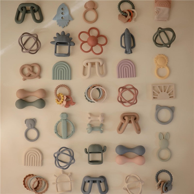 Mushie Silicone Lamb Figurine Teether, surrounded by various colorful silicone teethers and toys in different shapes.