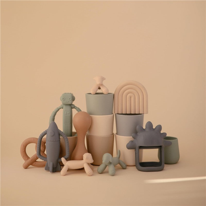 Silicone teething toys and stacking cups in soft pastel colors, including lamb, rocket, and dinosaur shapes.