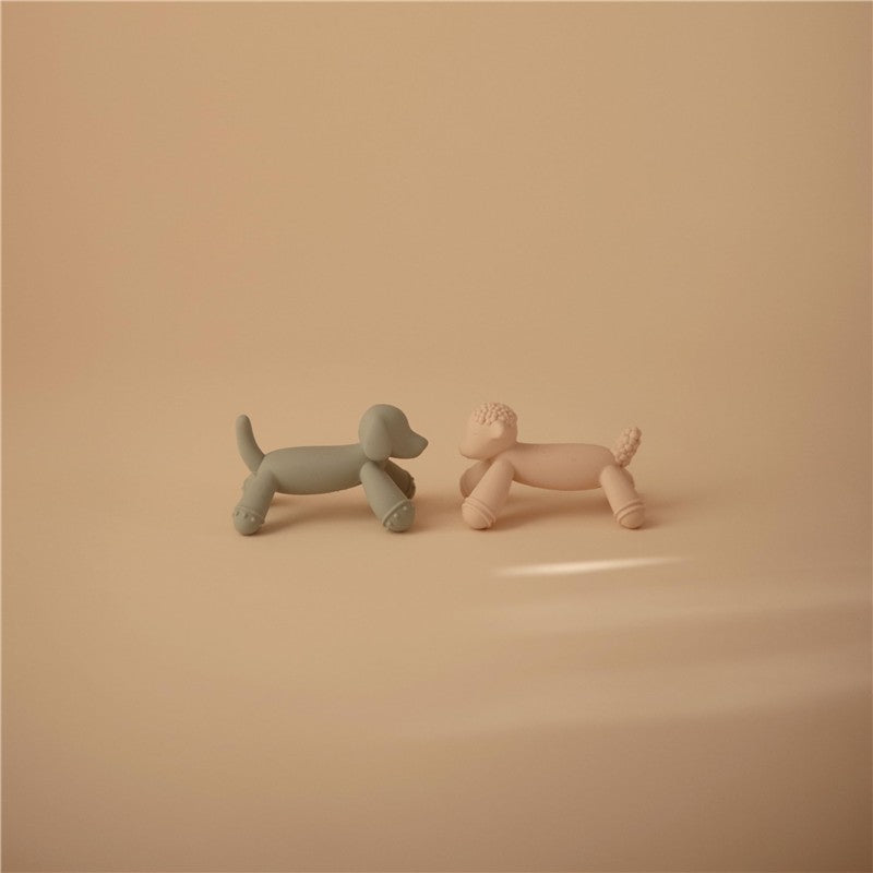 Silicone figurine teethers shaped like two playful dogs, one green and one pink, against a soft beige background.