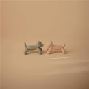 Silicone figurine teethers shaped like two playful dogs, one green and one pink, against a soft beige background.