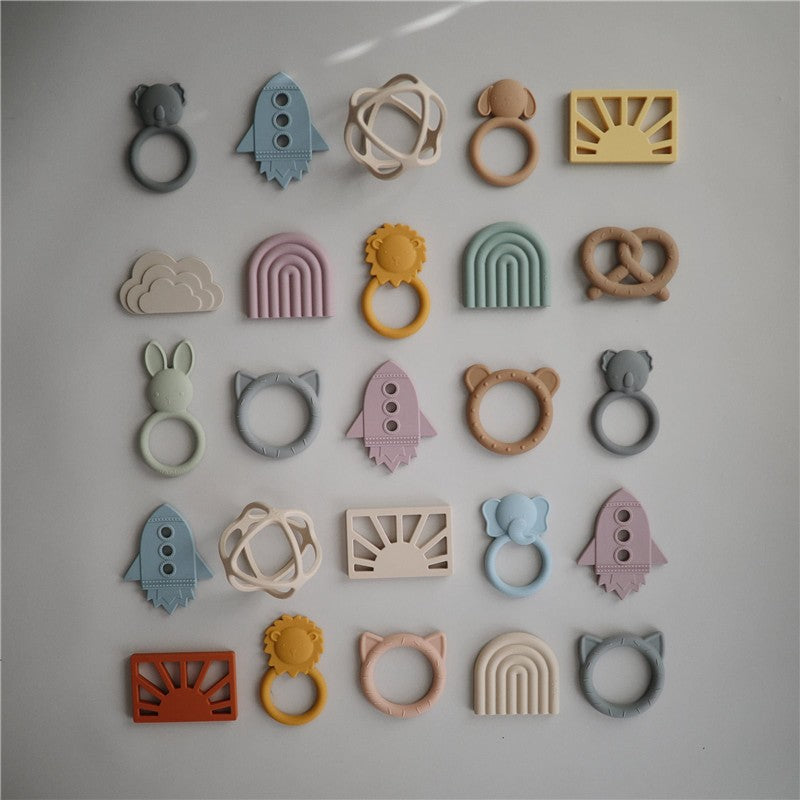 Mushie Silicone Ball Teether in Woodchuck color, surrounded by various silicone teething toys in playful shapes and colors.