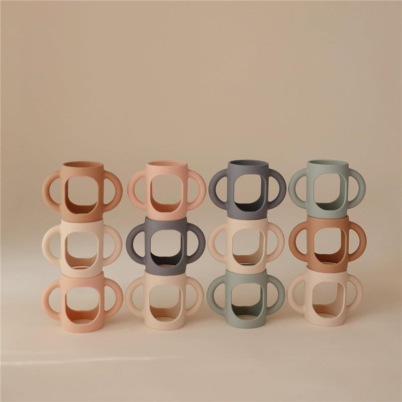 Silicone bottle handles in blush and shifting sand colors, designed for easy gripping, displayed in a stacked arrangement.