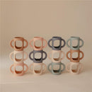 Silicone bottle handles in blush and shifting sand colors, designed for easy gripping, displayed in a stacked arrangement.