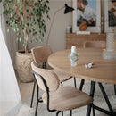Mushie Silicone Bottle Handles 2-Pack in Natural/Shifting Sand displayed on a wooden table with chairs and decor.