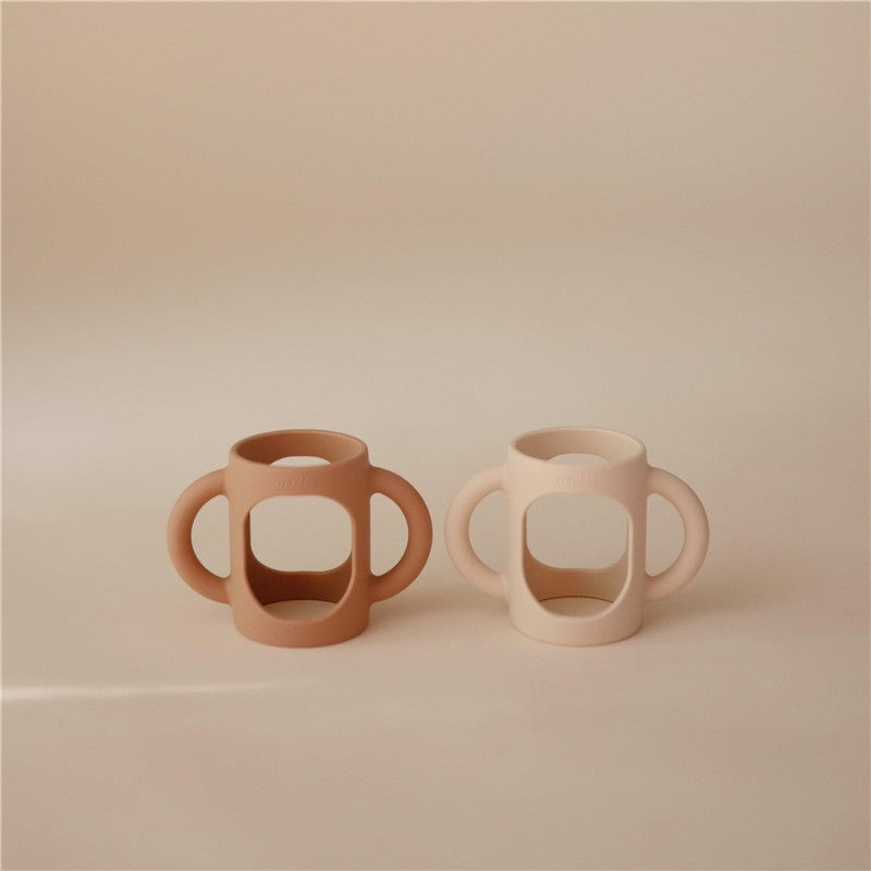 Silicone bottle handles in natural and shifting sand colors, designed for easy gripping by children.