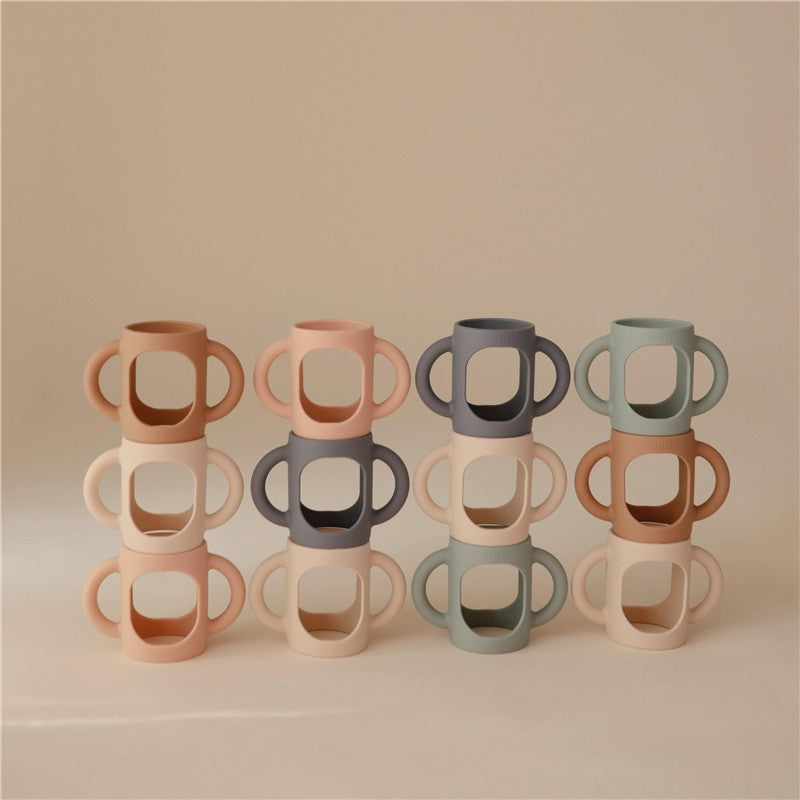 Mushie Silicone Bottle Handles in various colors, stacked in pairs, designed for easy grip by children.