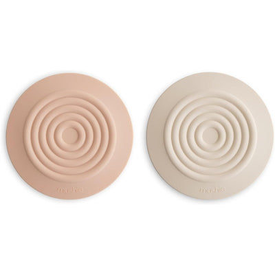 Silicone drain stoppers in blush and shifting sand colors, featuring concentric ring designs.