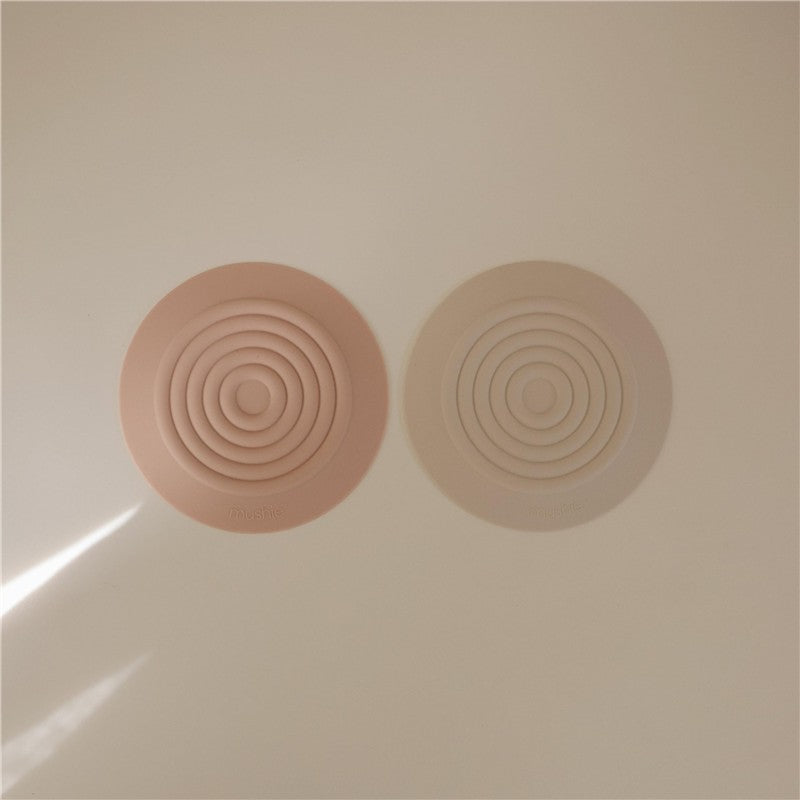 Silicone drain stoppers in blush and shifting sand colors, featuring concentric circle designs.
