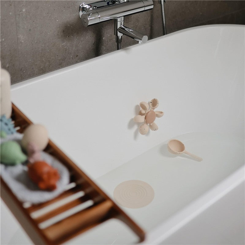 Mushie Silicone Drain Stopper 2-Pack in Blush and Shifting Sand, featuring flower and circular designs, in a bathtub.