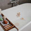 Mushie Silicone Drain Stopper 2-Pack in Blush and Shifting Sand, featuring flower and circular designs, in a bathtub.