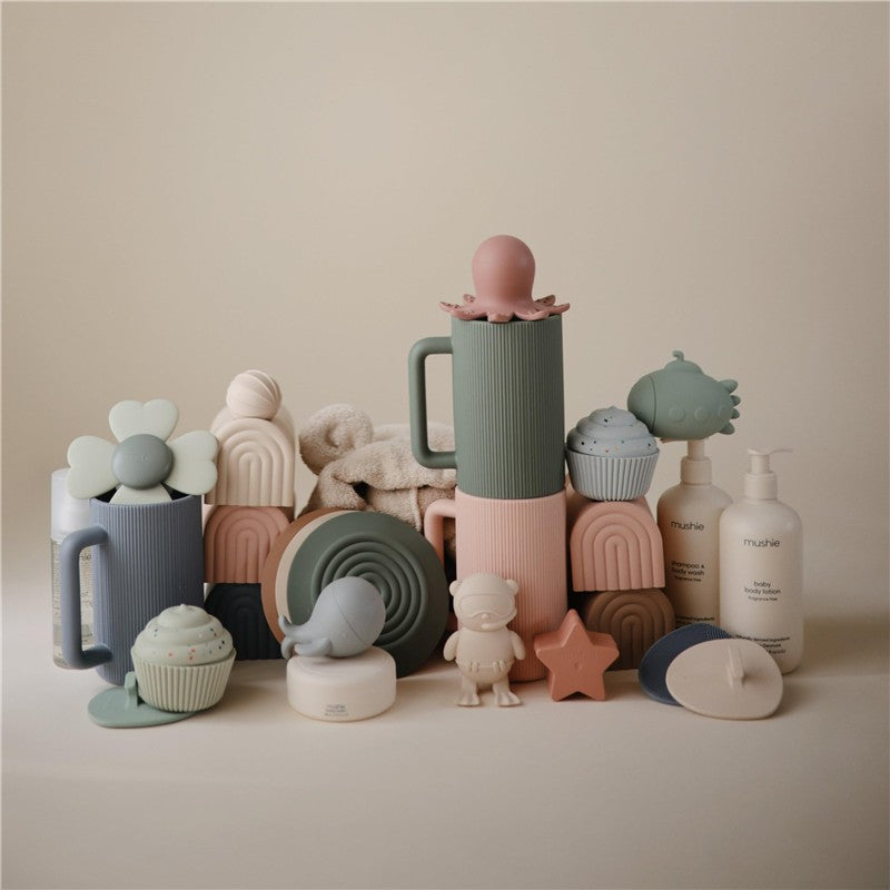 Silicone drain stoppers in blush and shifting sand colors, featuring playful designs and various shapes.